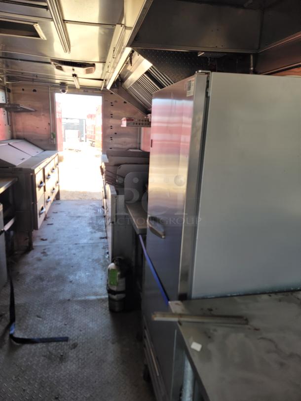 Interior of a commercial food truck, featuring stainless steel appliances, a refrigerator, stove, and exhaust hood.