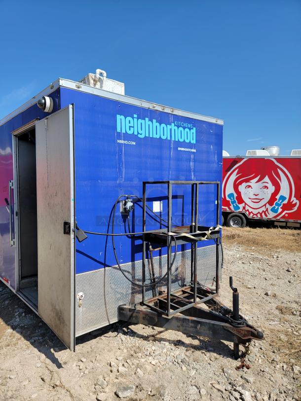 Blue food trailer labeled "Neighborhood Kitchens" with towing hitch, open side door, and visible ventilation. Good exterior condition.