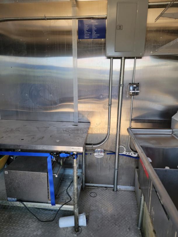 Industrial kitchen setup with a stainless steel countertop, electrical panel, and sink. Visible wiring and conduit along the wall.