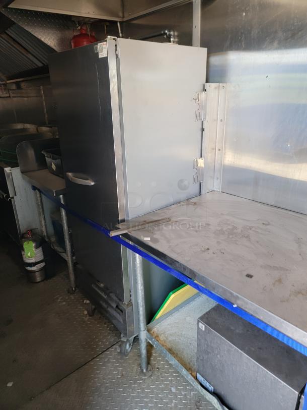 Commercial stainless steel kitchen oven with vertical handles, mounted on a wheeled metal frame. Visible scratches and wear.