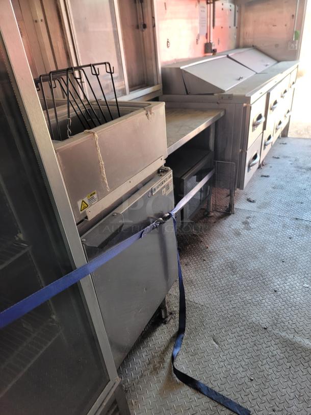 Commercial kitchen equipment inside a trailer, including stainless steel prep table, warming drawers, and storage area. Used condition.