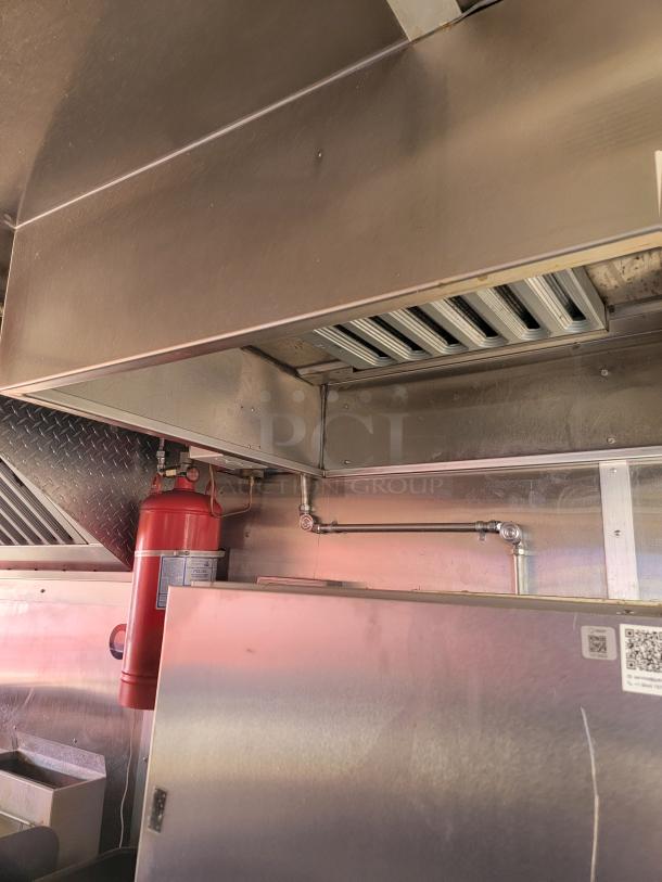 Commercial kitchen exhaust hood with fire suppression system, stainless steel construction, equipped with ventilation filters and fire extinguisher.