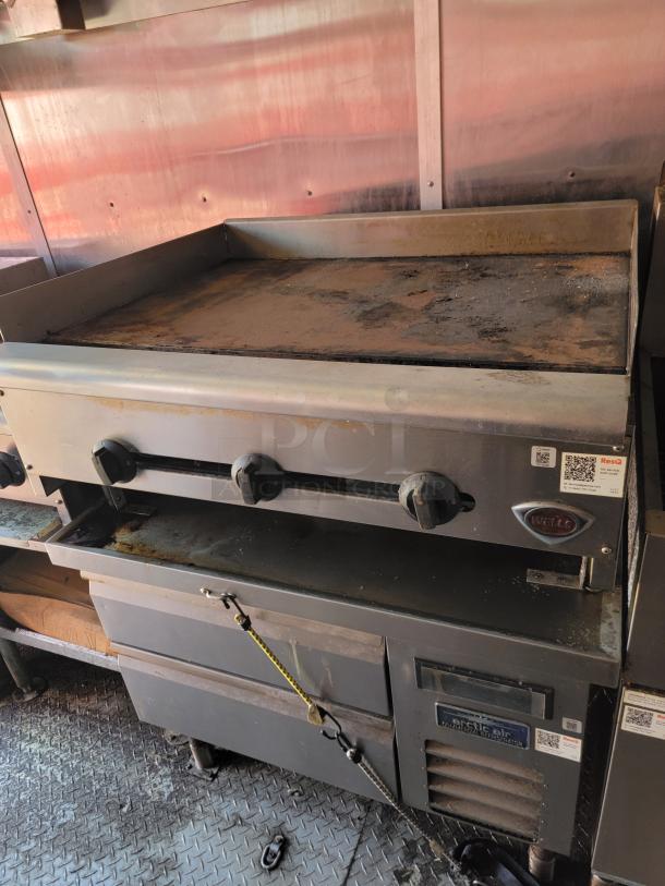 Commercial griddle with three control knobs and a rusty cooking surface, branded "Wells," with visible wear.