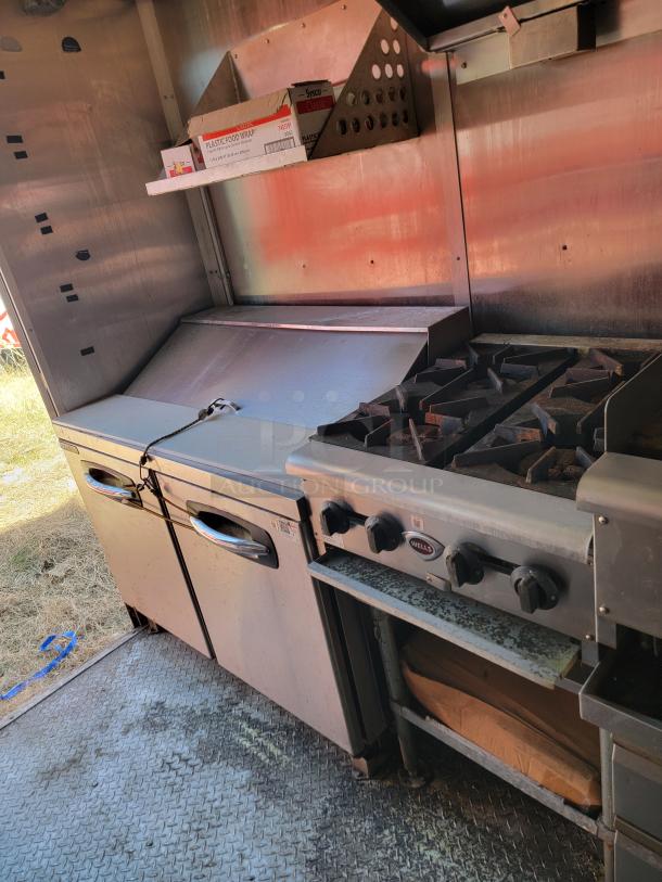Commercial kitchen setup with stainless steel equipment, including a griddle, storage area, and Wells stovetop. Visible signs of use.
