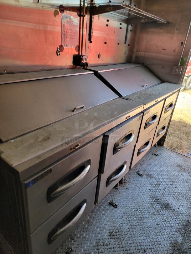 Commercial stainless steel food truck prep station with multiple drawers, large handles, and visible MBM sticker, showing mild wear.