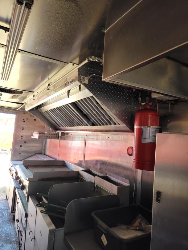 Commercial kitchen inside a food truck, featuring stainless steel appliances, grill, fryers, and ventilation system. Good condition.