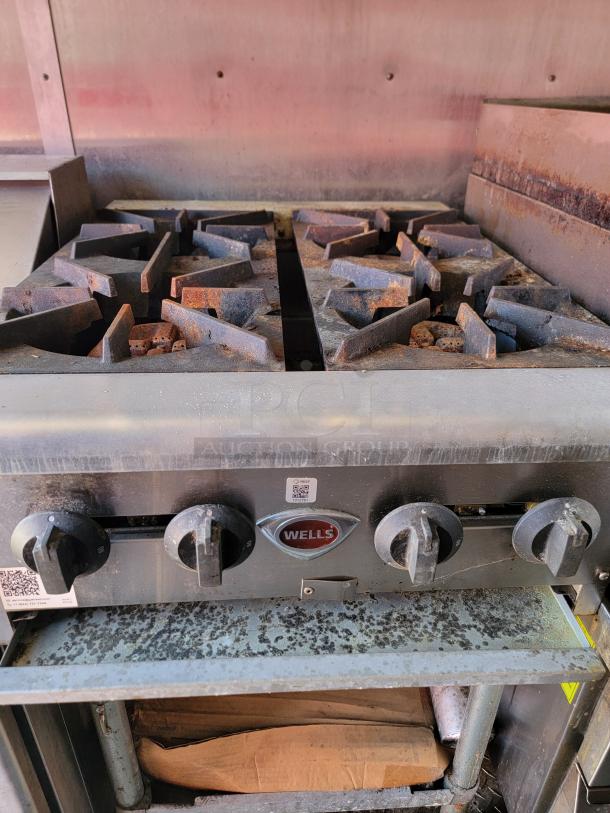 Wells commercial gas range with four burners, used condition, visible rust. Features control knobs, Wells branding on front.