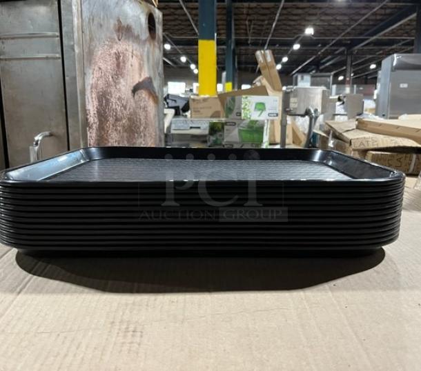 Brand new Carlisle CT141803 black 14"x18" fast food/serving tray. Stack of trays on a cardboard surface.