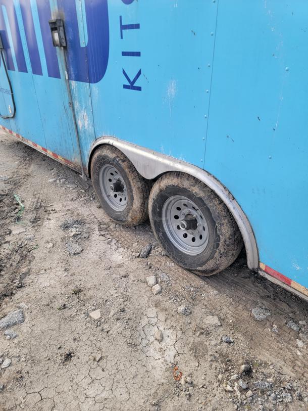Blue trailer with dual wheels on rough terrain. Weathered condition with visible dirt and scuff marks. Text reads "KIT."