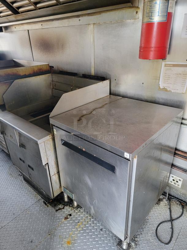 Commercial stainless steel fryer with visible wear, stains, and grease buildup, indicating heavy use. Fire extinguisher and safety labels present.