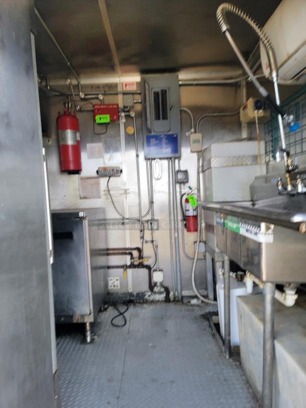 Industrial kitchen setup with stainless steel appliances, fire extinguisher, and visible piping. Used condition, suitable for catering business.