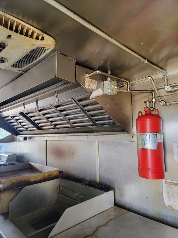 Commercial kitchen ventilation system with overhead exhaust, fryer, and red fire extinguisher. Visible label details safety specifications.