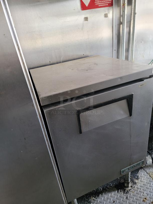 Stainless steel undercounter refrigerator, good condition, with visible True brand label, ergonomic handle, and sturdy legs.