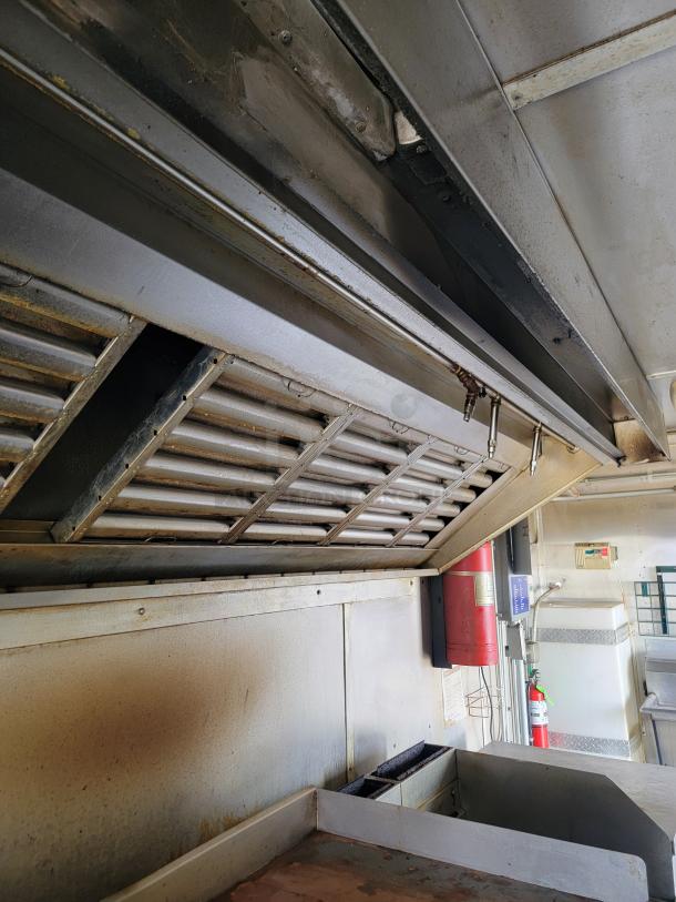 Commercial kitchen exhaust hood with ventilation system, showing signs of use and wear. Features fire suppression units.