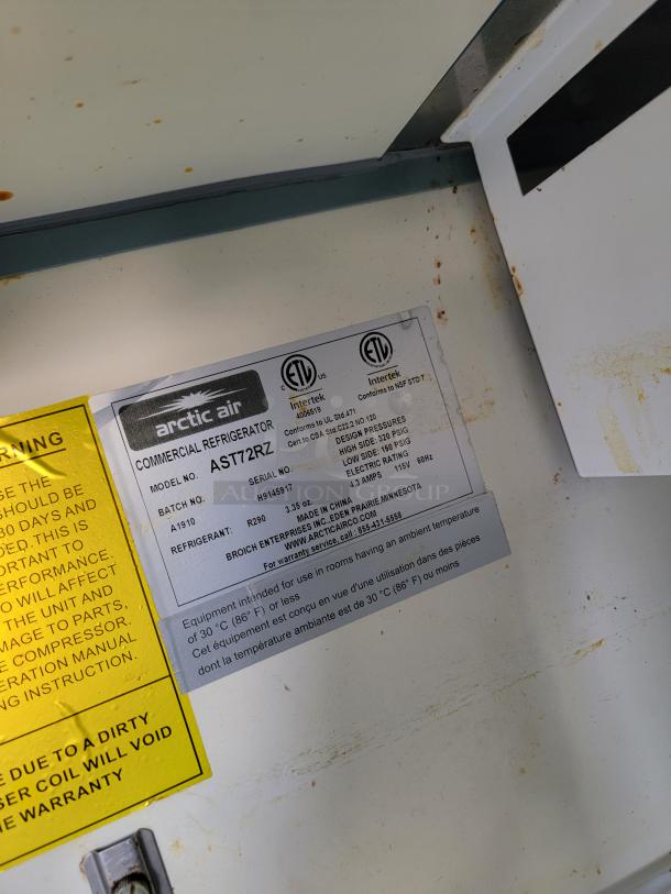 Arctic Air commercial refrigerator tag, model AST72R, showing specifications and safety warnings. Some rust stains visible.