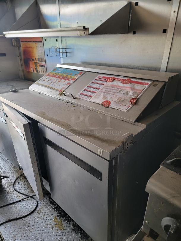 Industrial kitchen equipment with control panel, marked buttons, and instructional charts. Visible wear and metal construction.