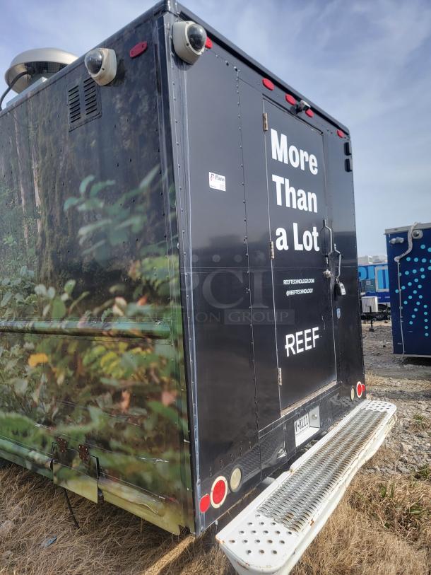 Mobile commercial unit by REEF with security cameras, logo, and "More Than a Lot" slogan. Features rear step and rugged exterior.