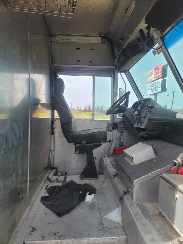 Interior view of a utility truck cabin featuring a driver's seat, steering wheel, and control panel. Metal flooring and storage compartments visible.