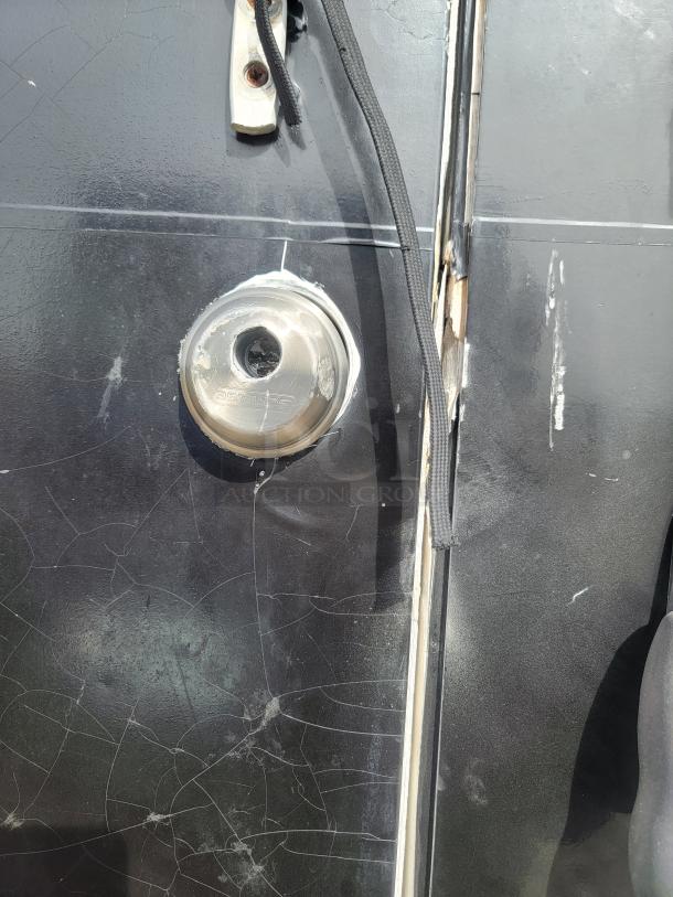 A black surface with a silver lock, showing signs of wear and scratches. Straps and mounting bracket are visible.