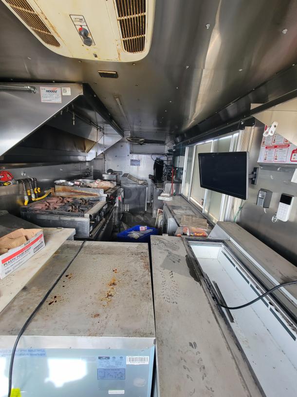 Interior of a used food truck kitchen with stainless steel appliances, ventilation hoods, and storage areas. Visible signs of wear.