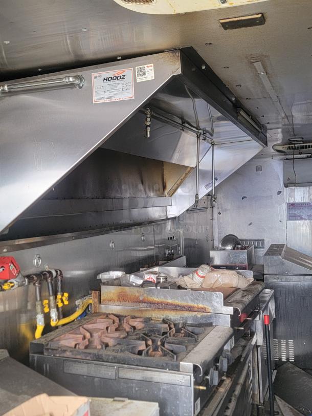 Commercial kitchen setup with exhaust hood, gas stove, and prep surfaces. Hoodz label on the exhaust. Used condition.
