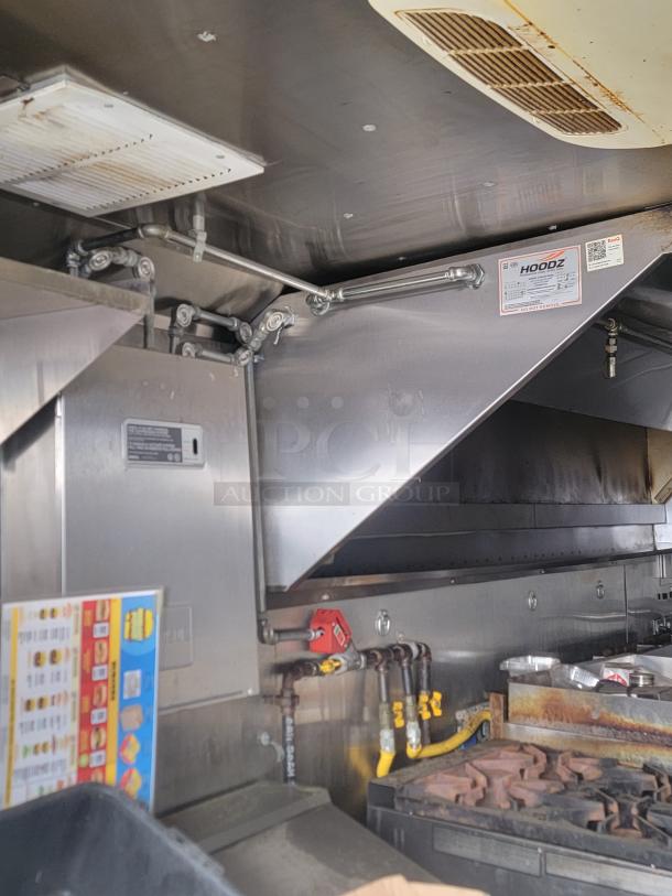 Commercial kitchen exhaust hood system in stainless steel, featuring HOODZ label with maintenance details. Includes venting and piping.
