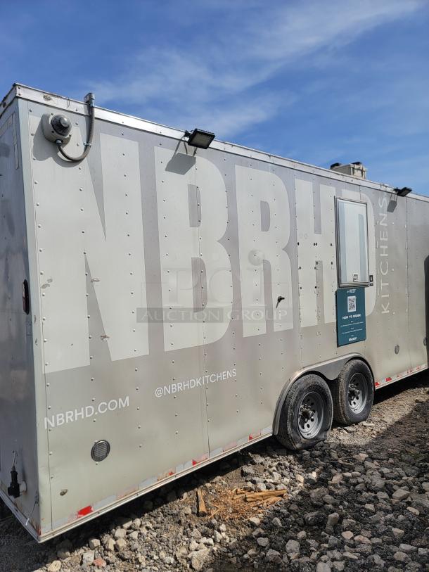Mobile kitchen trailer branded "NBRHD Kitchens," silver finish, dual axle, slight wear. Features external lighting and security camera.