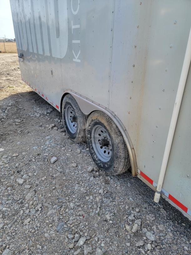 Dual-axle utility trailer with visible dirt on wheels and exterior, secured door, reflective tape, and legible brand markings.