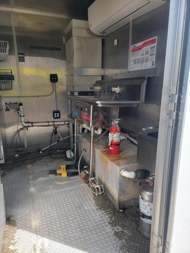 Industrial kitchen setup with stainless steel sink, overhead power unit, and fire extinguisher. Condition shows wear.
