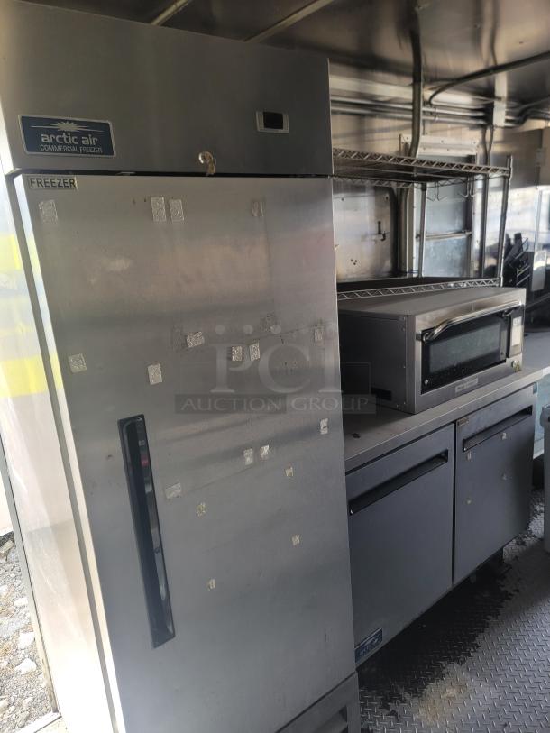 Arctic Air commercial freezer with stainless steel finish, visible wear, front handle, and label indicating it is a freezer.