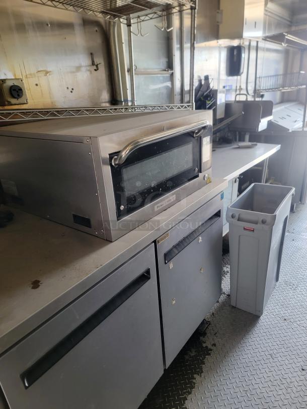 Stainless steel commercial oven with glass window and handle, set on a counter. Some wear visible. Industrial kitchen setting.