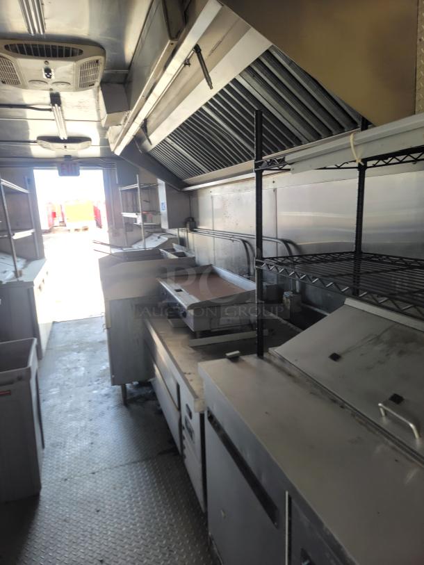 Commercial kitchen interior with stainless steel appliances, exhaust hood, and shelving. Used condition, minor wear visible.