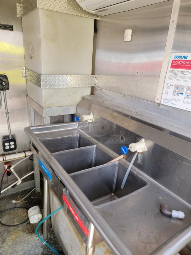 Commercial three-compartment stainless steel sink with faucets, mounted in a utility area. Visible Ecolab Smartpower label.