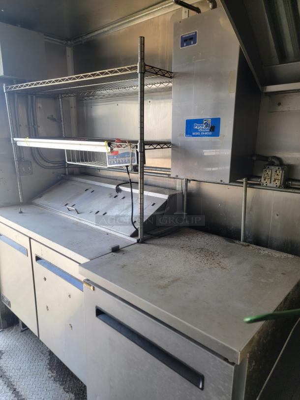 Commercial kitchen setup featuring a Pyro-Chem Model CM-4GU fire suppression unit and stainless steel prep station with shelving.