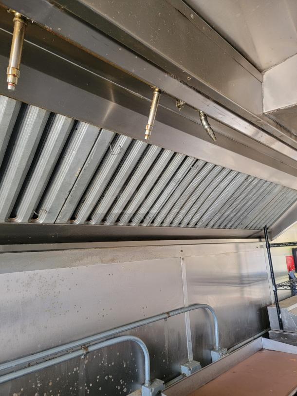 Commercial stainless steel kitchen hood with grease filters and fire suppression nozzles, showing grease stains; used condition.