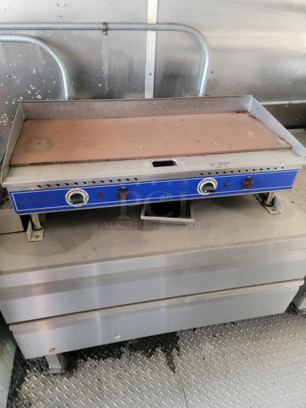 Commercial griddle with dual controls and blue front panel. Shows signs of use. Positioned on a metal counter.