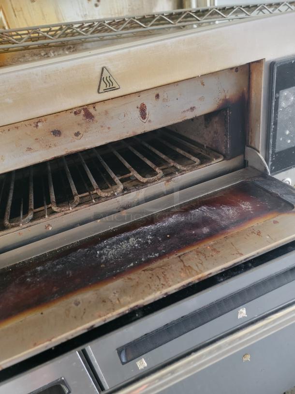 Industrial toaster, used, showing signs of rust and wear, with metal racks and caution heat symbol.