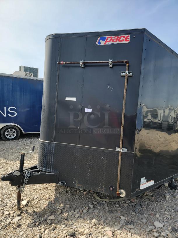 Black Pace trailer with diamond plate front panel, visible wear, and a logo. Features side door, hitch, and chain.