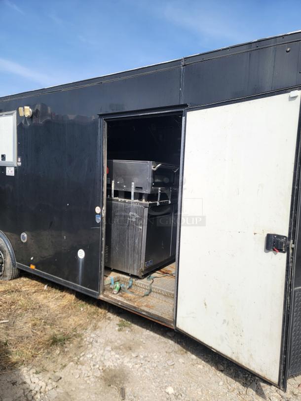 Black food trailer with side door open, revealing kitchen equipment. Exterior shows minor wear, suitable for mobile catering.