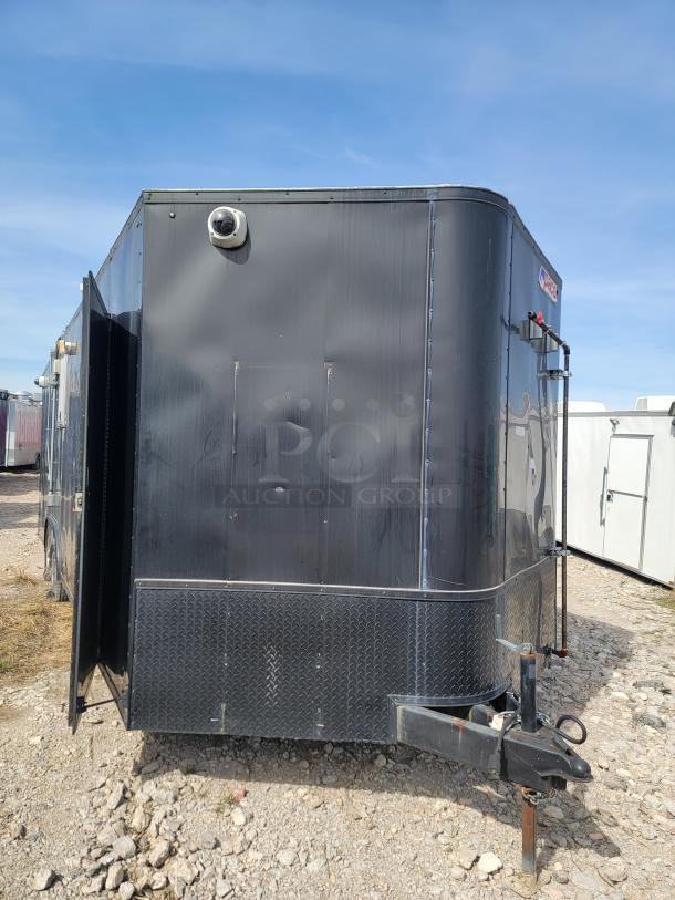 Black cargo trailer with diamond plate trim and mounted camera, showing minor wear. Suitable for various transport needs.