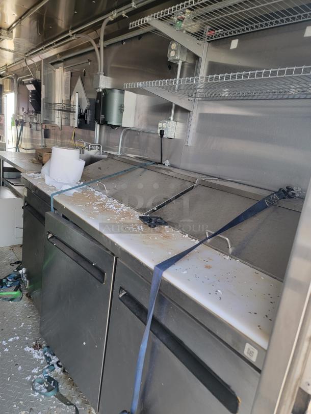 Commercial food truck interior with stainless steel prep stations, shelves, and visible wiring. Used condition with debris.