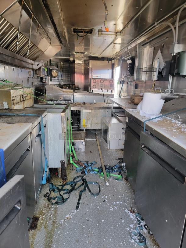 Commercial kitchen interior with stainless steel appliances, visible wear, and green straps. Equipment includes ovens and countertops.