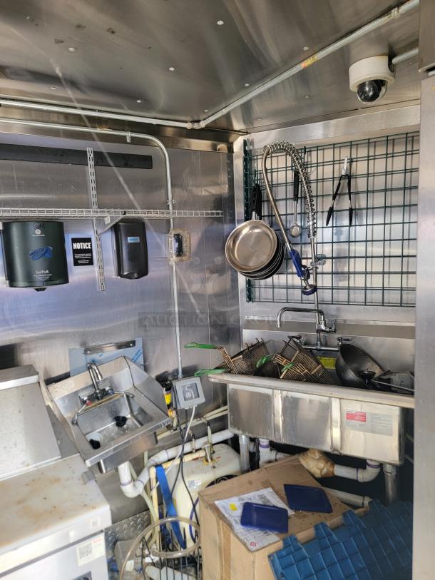 Commercial kitchen with stainless steel sink, faucet, frying baskets, and cleaning supplies. Notice on wall. Mixed condition.
