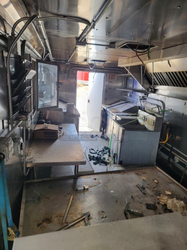 Interior view of a kitchen trailer with stainless steel countertops, storage shelves, and cooking equipment. Visible exit sign. Condition is used.