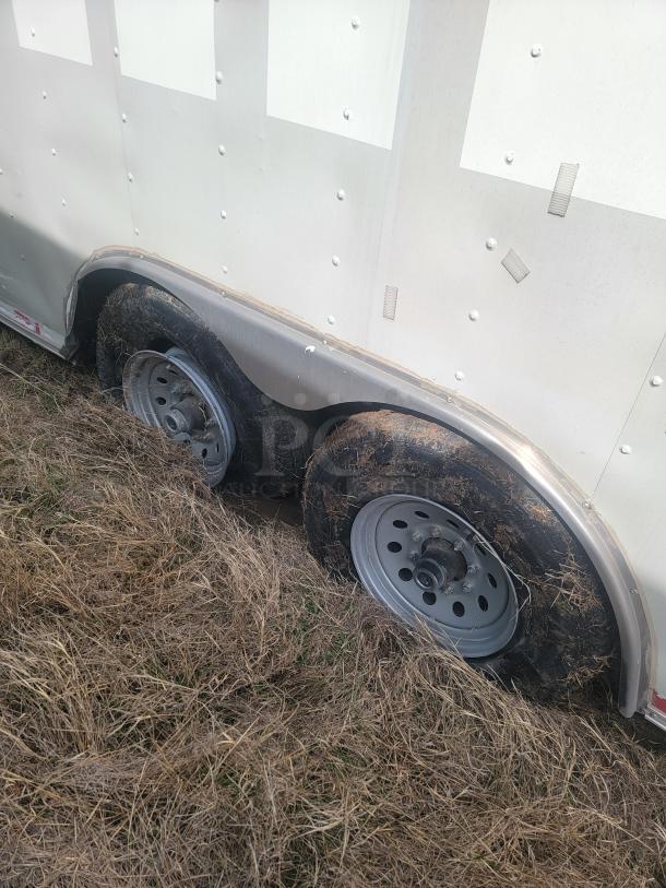 Dual axle enclosed trailer with visible wear and embedded in grass. Metal wheel rims and side panels with rivets.
