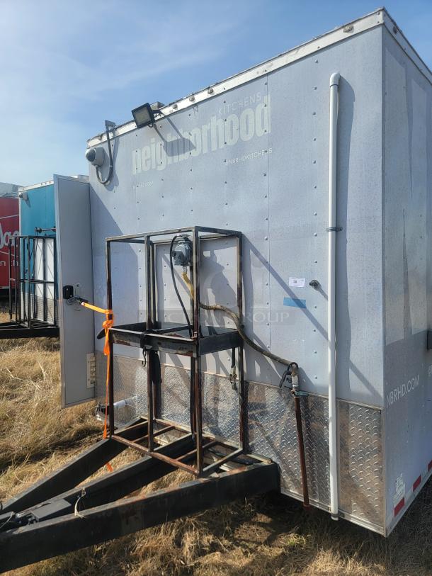 Mobile kitchen trailer with "Neighborhood Kitchens" branding. Features security camera, mounted light, and utility attachments. Weathered exterior.