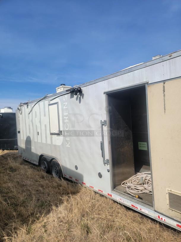 Mobile kitchen trailer with visible "KITCHENS" marking, dual axle, exterior wear, partially open door revealing storage interior.