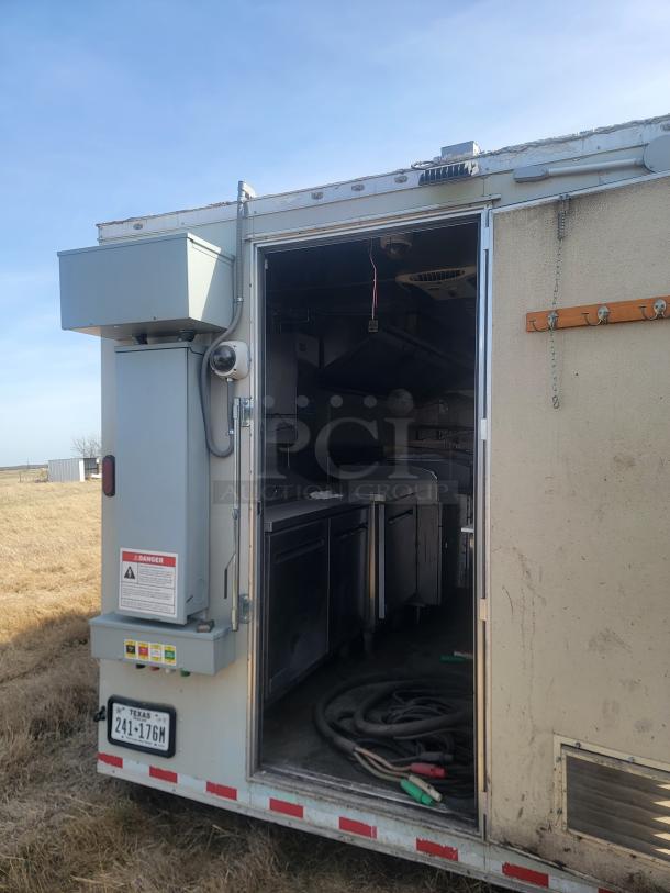 Mobile kitchen trailer with stainless steel interior appliances, utility cables, and equipment. Exterior condition shows wear.