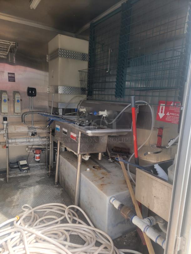 Commercial kitchen equipment in used condition. Features stainless steel sink, hoses, piping, and utility shelves. Visible signs of wear.