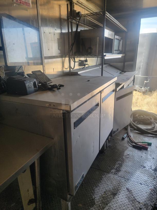 Commercial kitchen equipment including stainless steel countertop, shelves, and freezer units, in used condition.